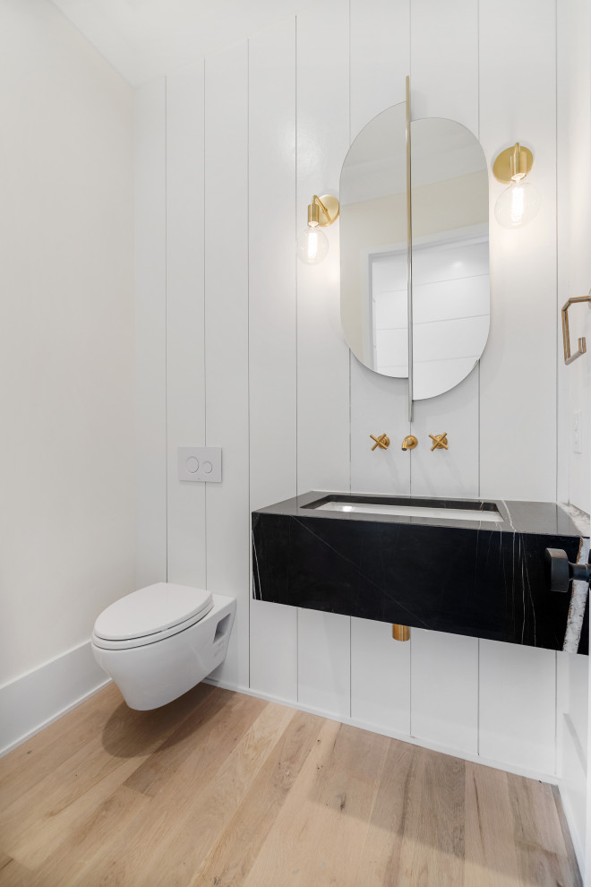Mid-sized modern powder room in Charleston with black cabinets, a wall-mount toilet, white walls, light hardwood floors, a wall-mount sink, black benchtops, a floating vanity and planked wall panelling.