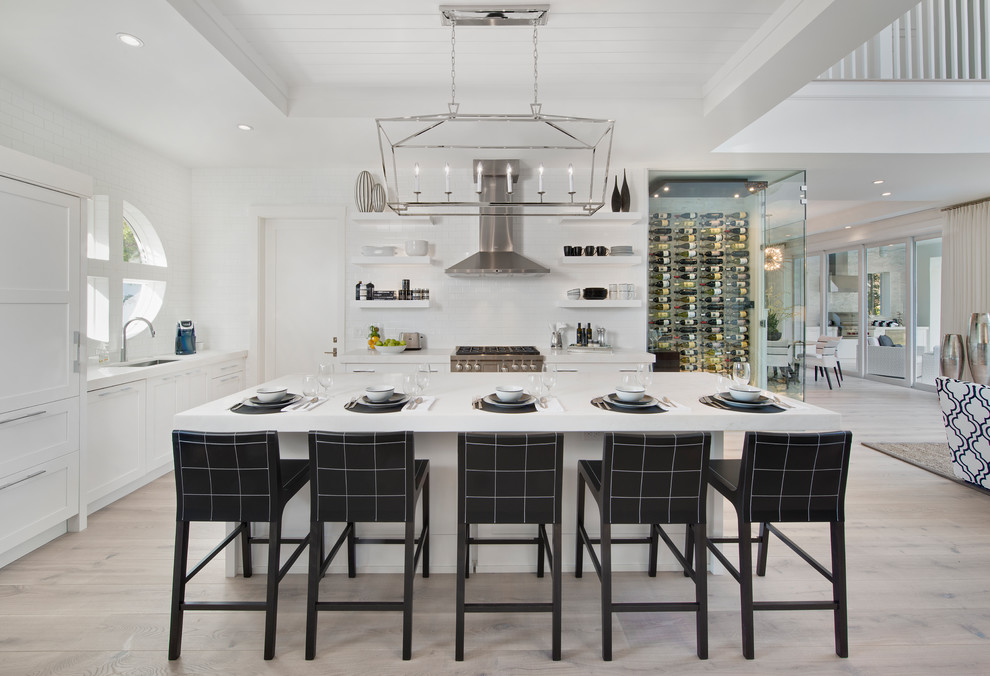 Photo of a transitional l-shaped open plan kitchen in Miami with an undermount sink, shaker cabinets, white cabinets, white splashback, stainless steel appliances, light hardwood floors, with island, beige floor and white benchtop.