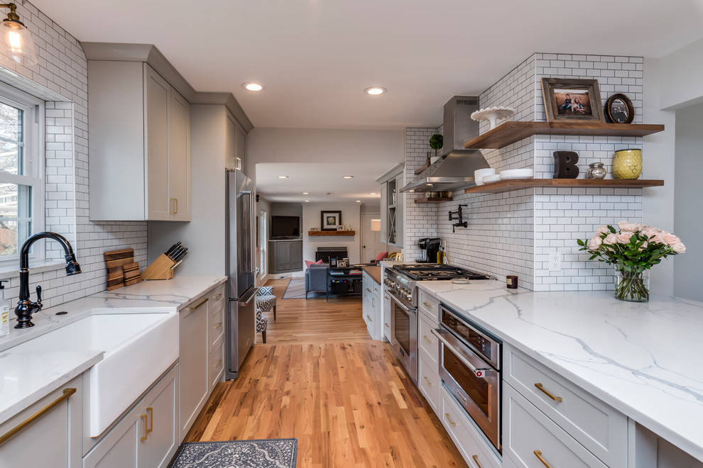 Inspiration for a mid-sized transitional galley medium tone wood floor eat-in kitchen remodel in Denver with a farmhouse sink, shaker cabinets, gray cabinets, quartz countertops, white backsplash, porcelain backsplash, stainless steel appliances, a peninsula and white countertops