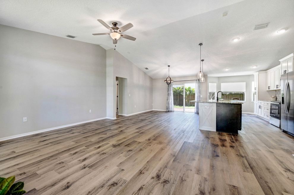 Example of a mid-sized country open concept vinyl floor, gray floor and vaulted ceiling living room design in Orlando with gray walls and no fireplace