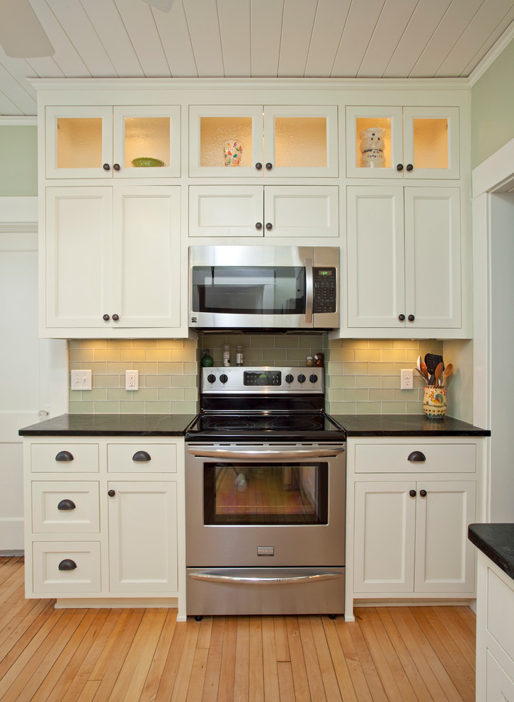 Design ideas for a small traditional separate kitchen in Minneapolis with an undermount sink, recessed-panel cabinets, white cabinets, soapstone benchtops, green splashback, glass tile splashback, stainless steel appliances, light hardwood floors, no island and beige floor.