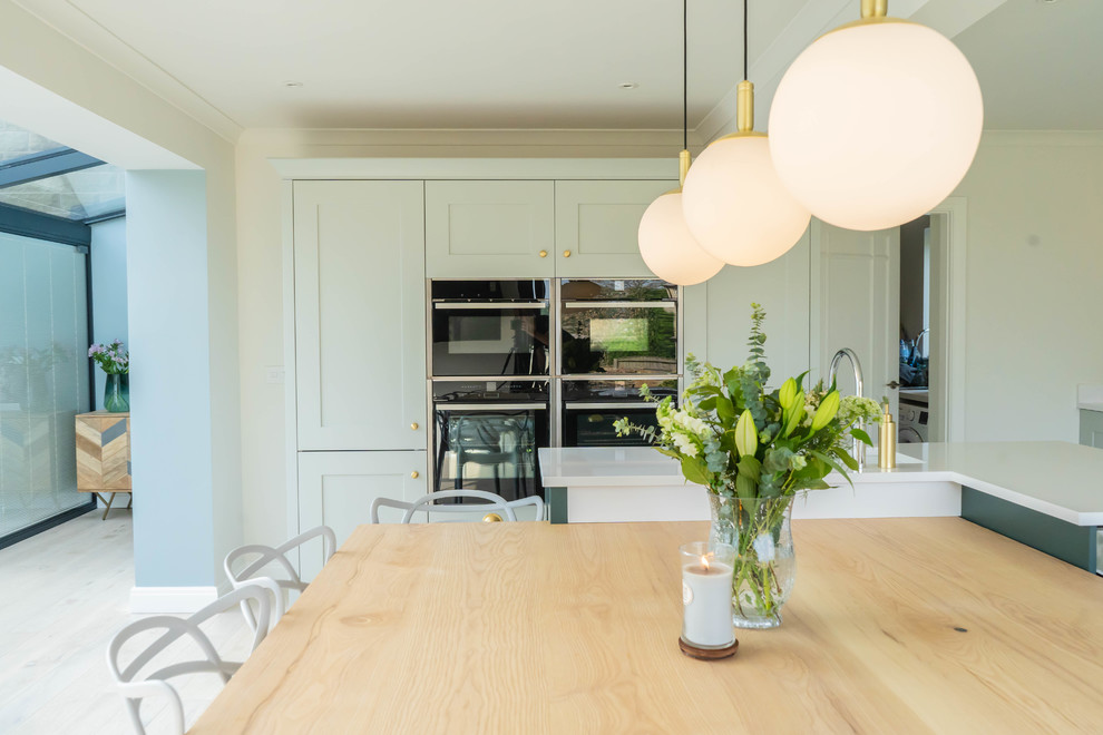 This is an example of a large contemporary l-shaped eat-in kitchen in Other with an undermount sink, shaker cabinets, green cabinets, quartzite benchtops, mirror splashback, panelled appliances, light hardwood floors, with island and white benchtop.