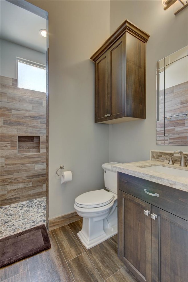 Mid-sized transitional 3/4 bathroom in Phoenix with recessed-panel cabinets, dark wood cabinets, a curbless shower, a two-piece toilet, beige tile, pebble tile, grey walls, medium hardwood floors, an undermount sink and granite benchtops.