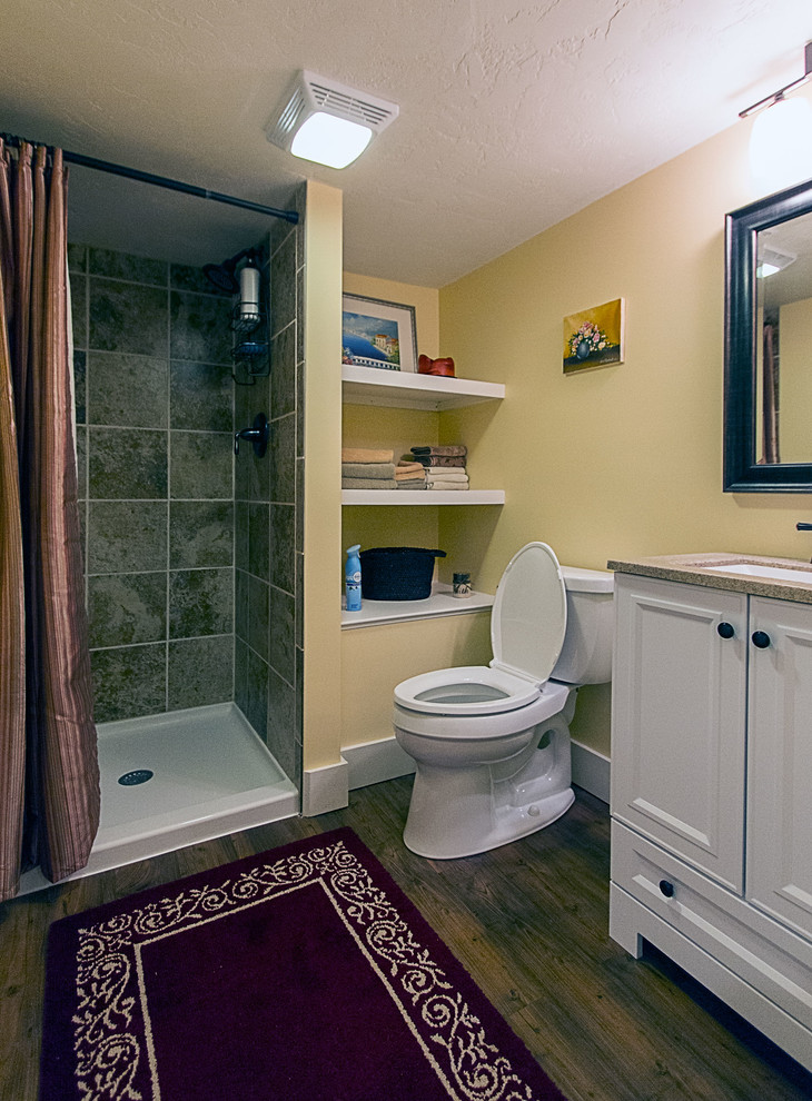 Example of a small transitional multicolored tile and porcelain tile alcove shower design with a console sink, flat-panel cabinets, white cabinets, solid surface countertops, a two-piece toilet, yellow walls and engineered wood floors