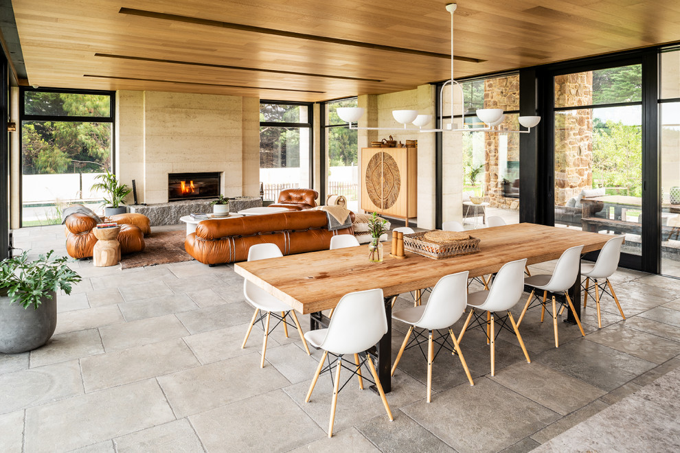 Cette image montre une grande salle à manger ouverte sur le salon design avec un mur beige, une cheminée standard, un sol gris et un plafond en bois.