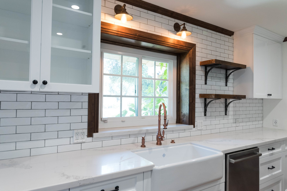 This is an example of an industrial kitchen in San Francisco with white cabinets, quartzite benchtops, white splashback, ceramic splashback, stainless steel appliances, a farmhouse sink, cement tiles and brown floor.