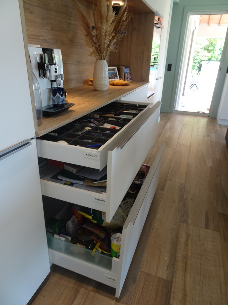 This is an example of a large modern single-wall open plan kitchen in Marseille with beaded inset cabinets, white cabinets, laminate benchtops, beige splashback, medium hardwood floors, with island and beige benchtop.