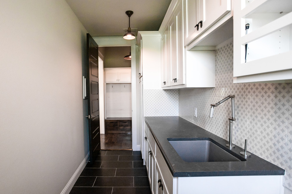 Design ideas for a large modern single-wall utility room in Dallas with an undermount sink, shaker cabinets, white cabinets, granite benchtops, grey walls, ceramic floors, a side-by-side washer and dryer and black floor.