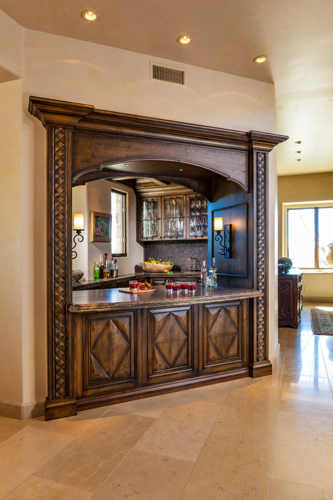 Photo of a large traditional u-shaped home bar in Phoenix with an undermount sink, raised-panel cabinets, medium wood cabinets, granite benchtops, multi-coloured splashback, limestone floors and beige floor.