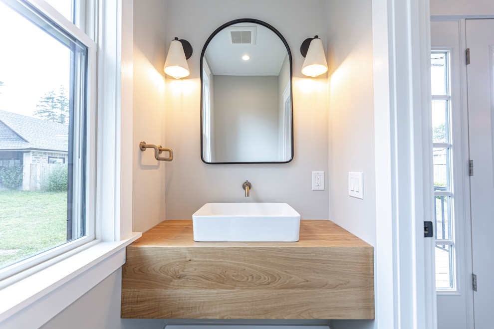 Country powder room in Philadelphia with light wood cabinets, a one-piece toilet, beige walls, ceramic floors, a vessel sink, wood benchtops, grey floor and a floating vanity.