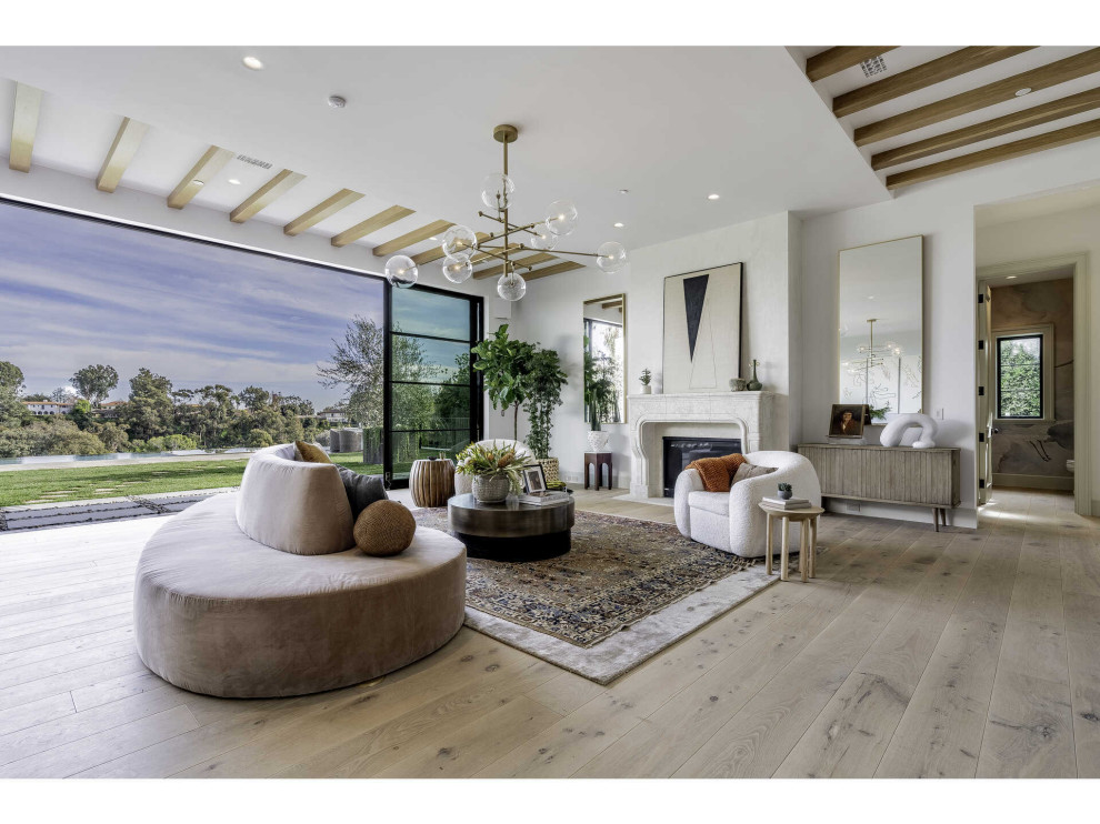 Expansive contemporary open concept living room in Los Angeles with light hardwood floors, a standard fireplace, a stone fireplace surround, no tv and white walls.