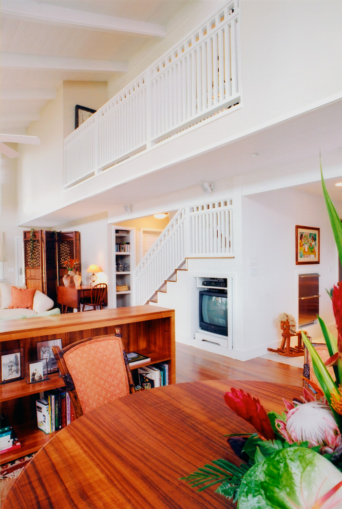 This is an example of a small country loft-style living room in Hawaii with white walls, medium hardwood floors, a corner fireplace, a stone fireplace surround and a concealed tv.