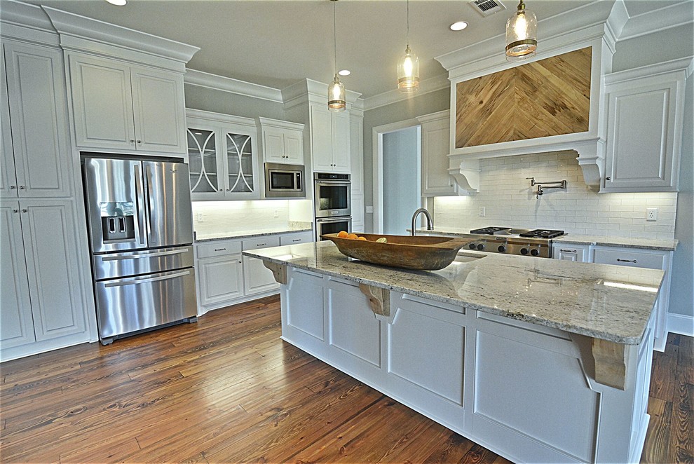 Inspiration for a large transitional l-shaped dark wood floor and brown floor enclosed kitchen remodel in Jackson with an undermount sink, raised-panel cabinets, white cabinets, granite countertops, white backsplash, stone tile backsplash, stainless steel appliances and an island