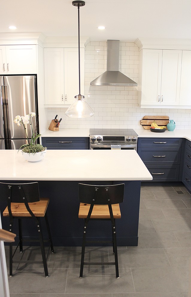 Example of a large transitional l-shaped porcelain tile enclosed kitchen design in Toronto with an undermount sink, recessed-panel cabinets, white cabinets, solid surface countertops, white backsplash, ceramic backsplash, stainless steel appliances and an island