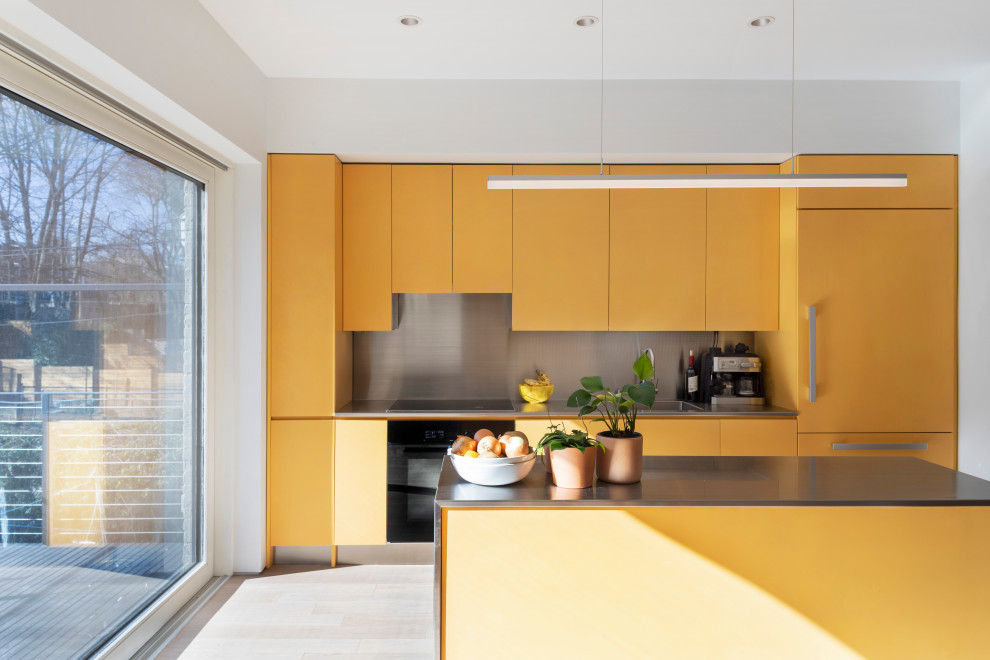 Zweizeilige Moderne Küche mit flächenbündigen Schrankfronten, gelben Schränken, Küchenrückwand in Grau, hellem Holzboden, Kücheninsel, beigem Boden, grauer Arbeitsplatte und Elektrogeräten mit Frontblende in New York