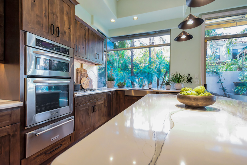 Inspiration for a large transitional u-shaped open concept kitchen remodel in Phoenix with a farmhouse sink, shaker cabinets, dark wood cabinets, quartz countertops, white backsplash, quartz backsplash, stainless steel appliances, an island and white countertops
