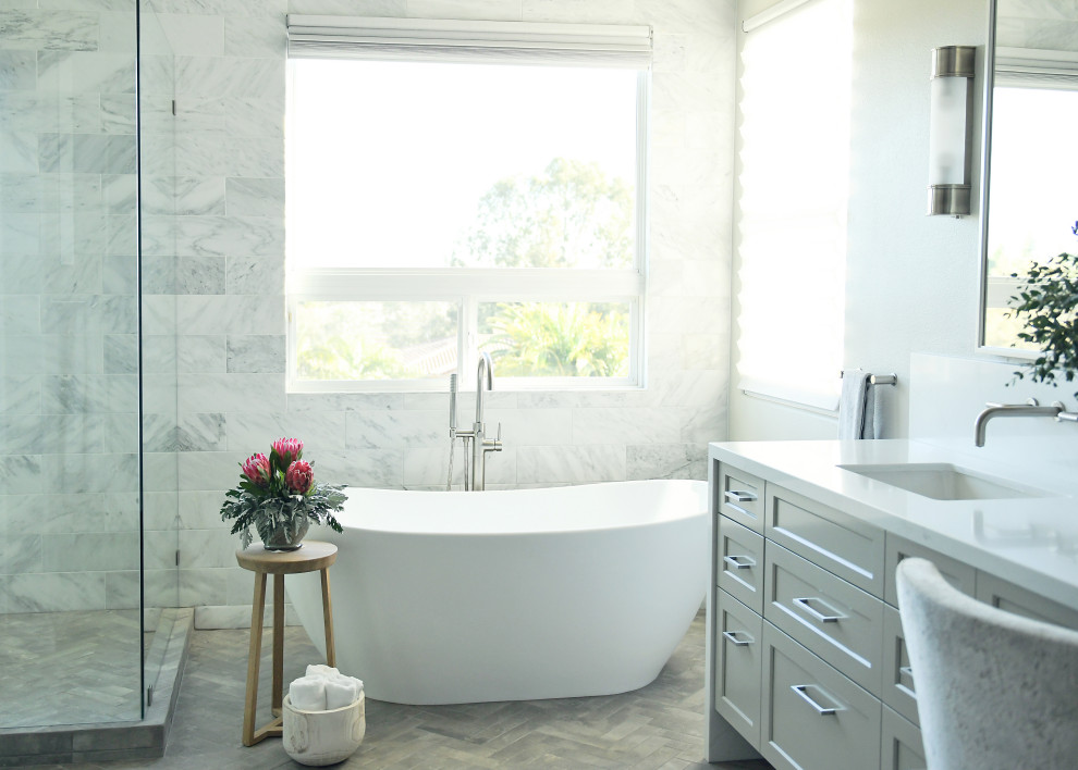 This is an example of a large transitional master bathroom in San Diego with shaker cabinets, grey cabinets, a freestanding tub, a double shower, a one-piece toilet, white tile, marble, grey walls, porcelain floors, an undermount sink, engineered quartz benchtops, grey floor, a hinged shower door, white benchtops, an enclosed toilet, a double vanity and a built-in vanity.