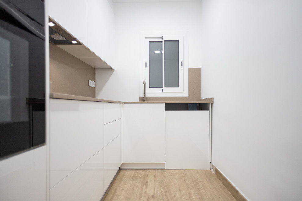 Design ideas for a mid-sized contemporary l-shaped separate kitchen in Barcelona with a single-bowl sink, flat-panel cabinets, white cabinets, beige splashback, black appliances, ceramic floors, no island, brown floor and beige benchtop.