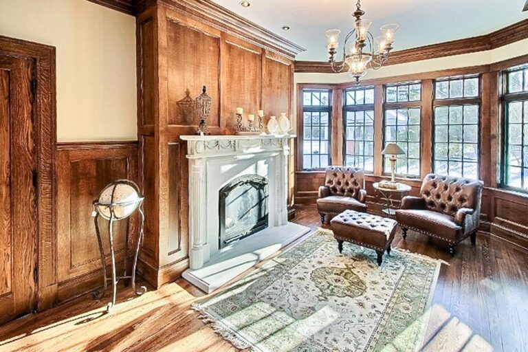 Photo of a mid-sized traditional enclosed family room in Cleveland with a library, beige walls, dark hardwood floors, a standard fireplace, a wood fireplace surround, brown floor and decorative wall panelling.