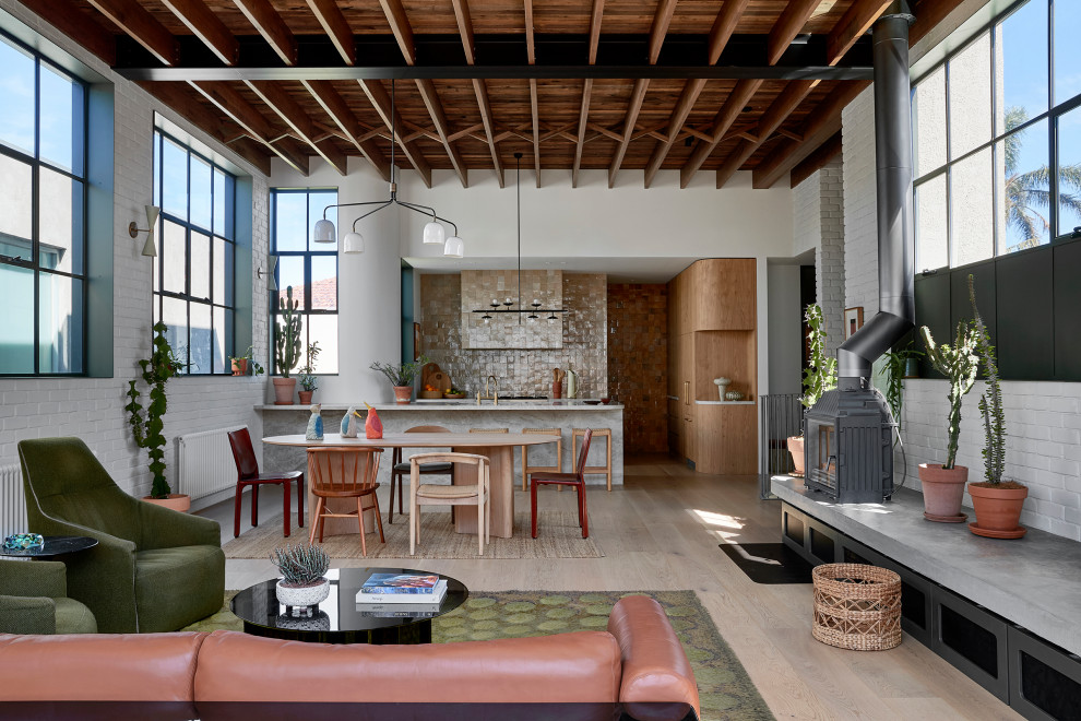 Design ideas for a mid-sized industrial open concept living room in Melbourne with white walls, light hardwood floors, a wood stove and beige floor.