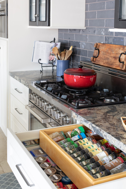Freestanding gas range between white kitchen cabinets with open spice drawer and red Dutch oven on cooktop