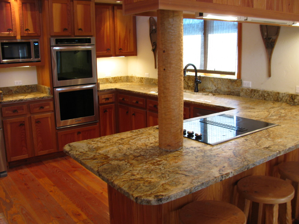 Example of a medium tone wood floor eat-in kitchen design with an undermount sink, granite countertops and stone slab backsplash
