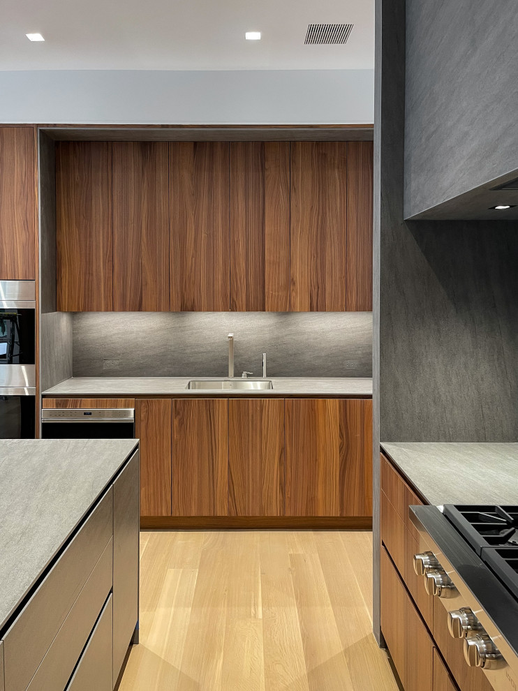 Design ideas for an expansive modern u-shaped eat-in kitchen in New York with an undermount sink, flat-panel cabinets, medium wood cabinets, grey splashback, panelled appliances, light hardwood floors, with island and grey benchtop.