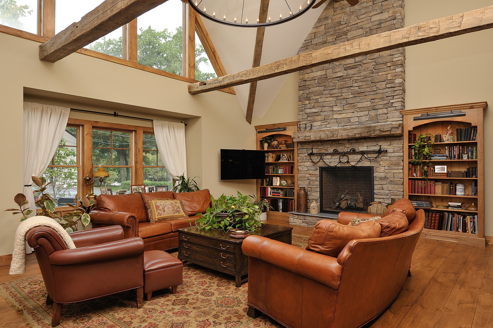 This is an example of a mid-sized country living room in Other with beige walls, a standard fireplace, a stone fireplace surround, a library, medium hardwood floors, a wall-mounted tv and brown floor.