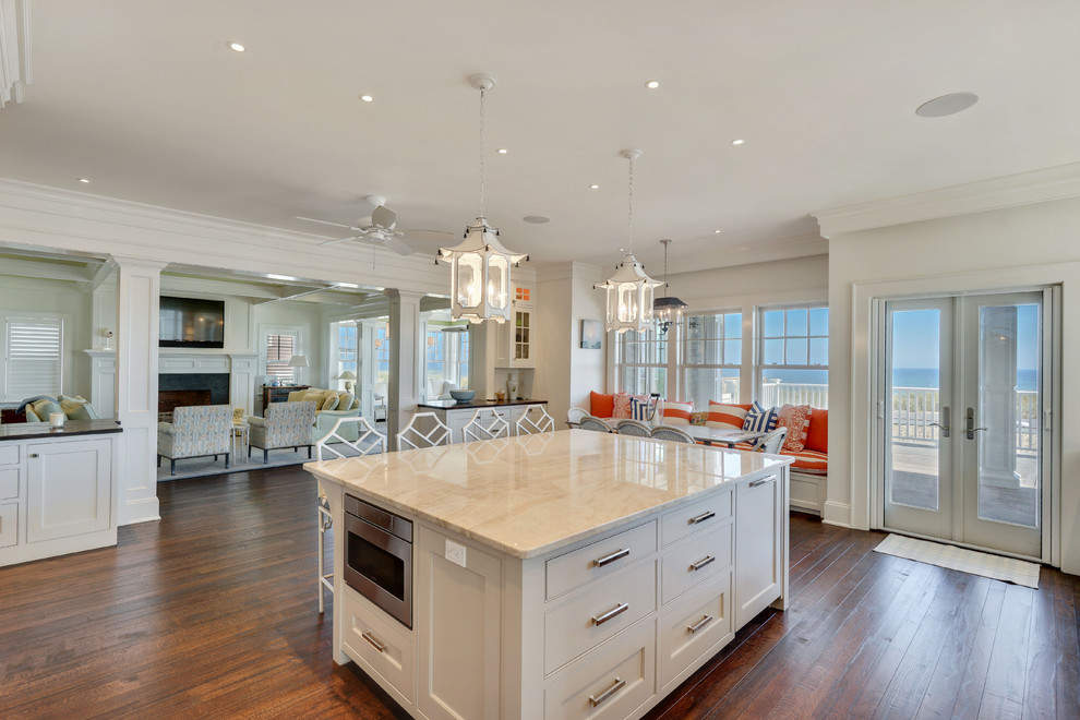 Photo of an expansive beach style u-shaped kitchen in New York with white cabinets, granite benchtops, stainless steel appliances, dark hardwood floors, with island, brown floor and white benchtop.