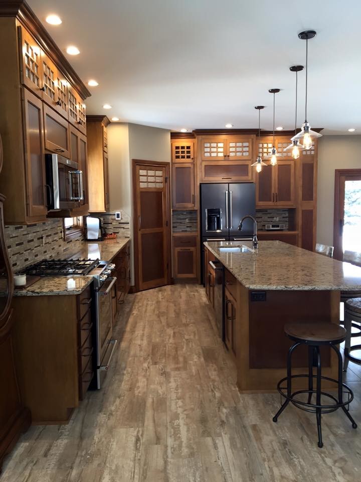 Example of a large transitional l-shaped eat-in kitchen design with a single-bowl sink, brown cabinets, granite countertops, brown backsplash, stainless steel appliances and an island
