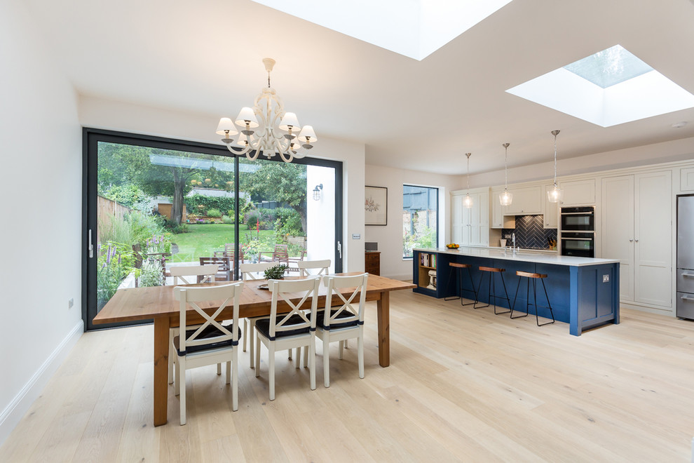 Photo of a large contemporary kitchen/dining combo in London with white walls and light hardwood floors.