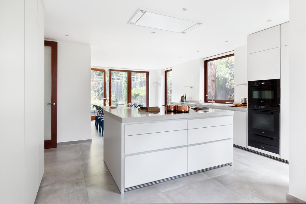 Mid-sized contemporary galley eat-in kitchen in London with an integrated sink, flat-panel cabinets, white cabinets, quartz benchtops, white splashback, black appliances, ceramic floors and with island.