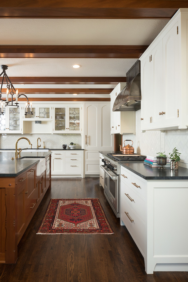 Design ideas for a traditional l-shaped kitchen in Minneapolis with a farmhouse sink, shaker cabinets, white cabinets, white splashback, stainless steel appliances, dark hardwood floors, with island, brown floor and black benchtop.