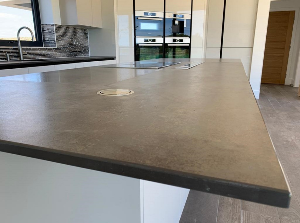 Large modern l-shaped open plan kitchen in Dorset with an integrated sink, flat-panel cabinets, white cabinets, quartzite benchtops, grey splashback, cement tile splashback, stainless steel appliances, with island and grey benchtop.