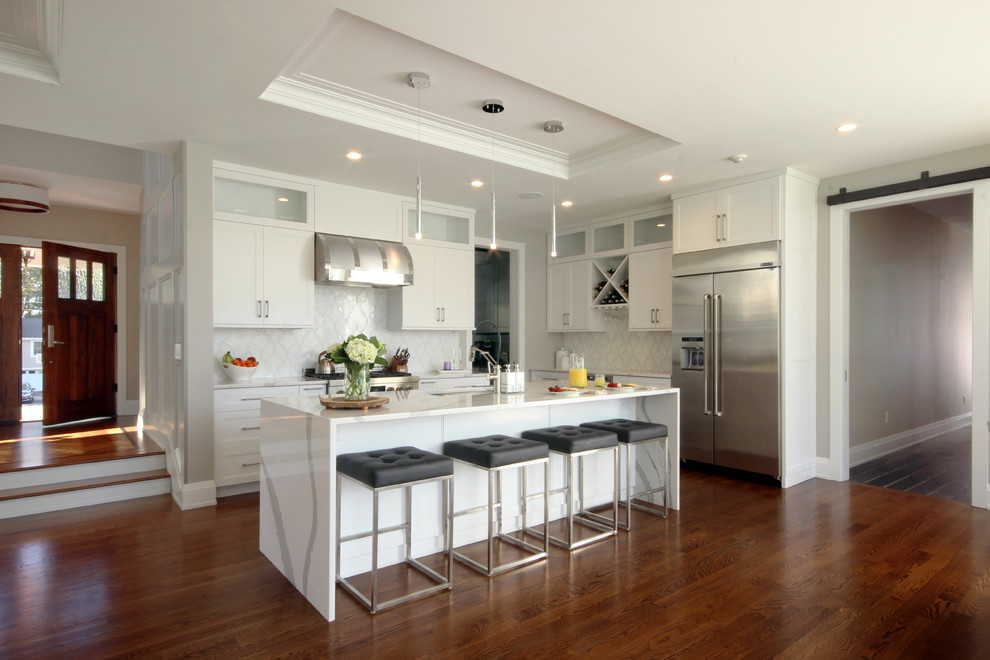 Inspiration for a transitional l-shaped kitchen in New York with an undermount sink, shaker cabinets, white cabinets, white splashback, stainless steel appliances, medium hardwood floors, with island and brown floor.