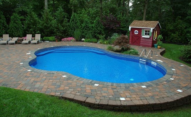 Photo of a Mid-sized american Backyard Custom-shaped Lap swimming pool in New York With Brick Pavers and a Pool House.