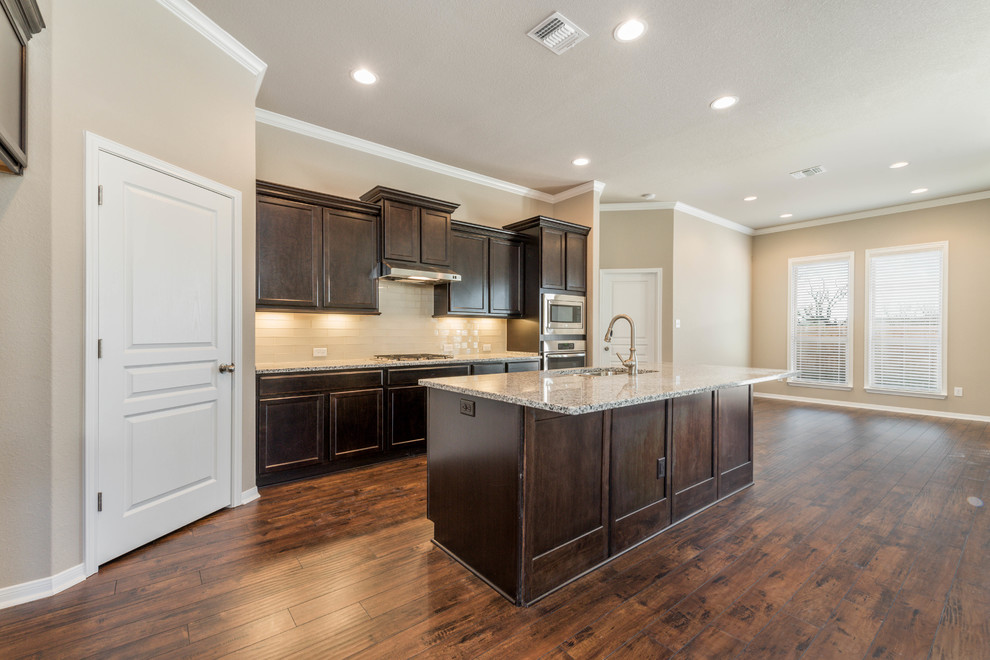 Large arts and crafts l-shaped open plan kitchen in Austin with an undermount sink, recessed-panel cabinets, dark wood cabinets, granite benchtops, beige splashback, subway tile splashback, stainless steel appliances, laminate floors, with island and brown floor.
