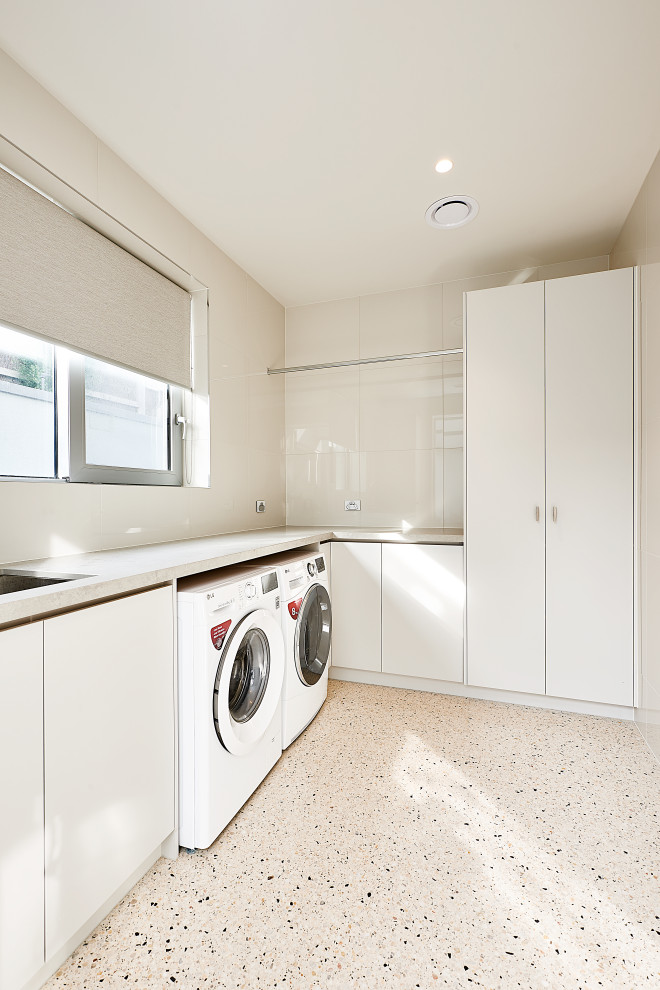 Photo of a modern single-wall dedicated laundry room in Melbourne with an undermount sink, flat-panel cabinets, beige cabinets, quartz benchtops, beige splashback, porcelain splashback, concrete floors, a side-by-side washer and dryer and grey benchtop.