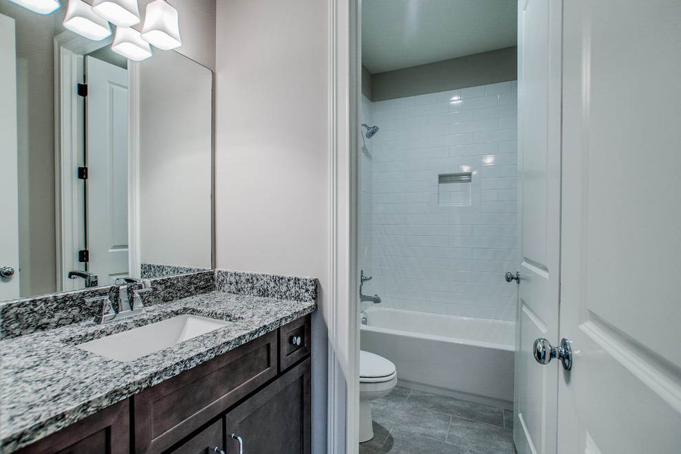 Photo of a mid-sized traditional bathroom in Nashville with shaker cabinets, dark wood cabinets, an alcove tub, a shower/bathtub combo, white tile, subway tile, yellow walls, porcelain floors, an undermount sink and granite benchtops.