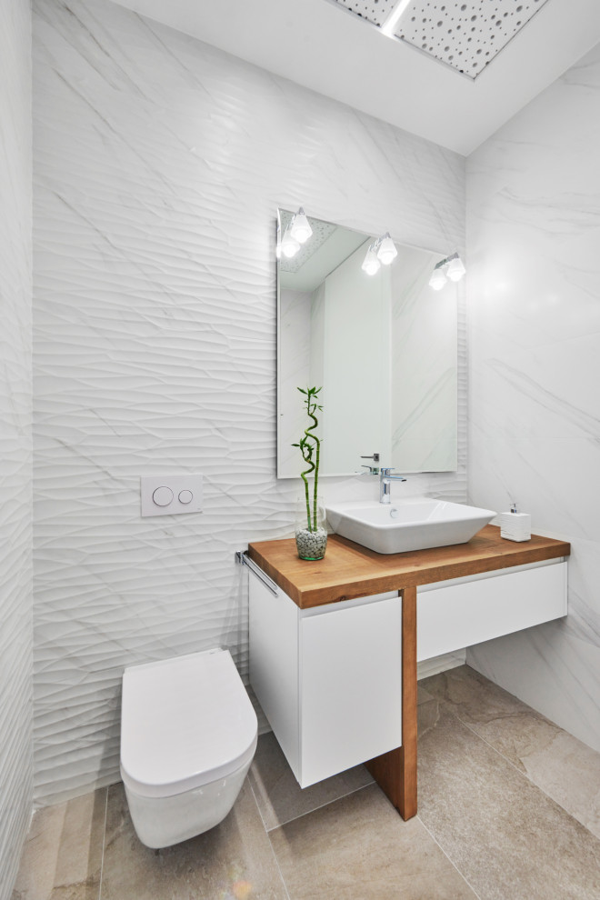 This is an example of a contemporary powder room in Other with flat-panel cabinets, white cabinets, a wall-mount toilet, white tile, a vessel sink, wood benchtops, beige floor, brown benchtops and a floating vanity.