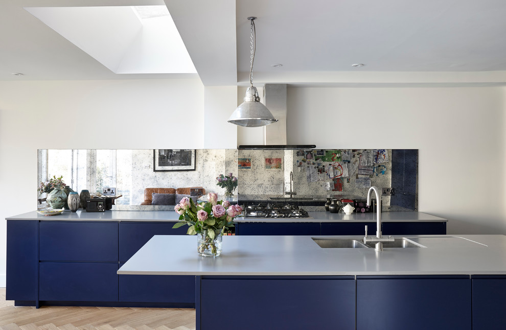 Inspiration for a mid-sized eclectic open plan kitchen in London with an undermount sink, flat-panel cabinets, blue cabinets, quartzite benchtops, metallic splashback, glass sheet splashback, stainless steel appliances and medium hardwood floors.