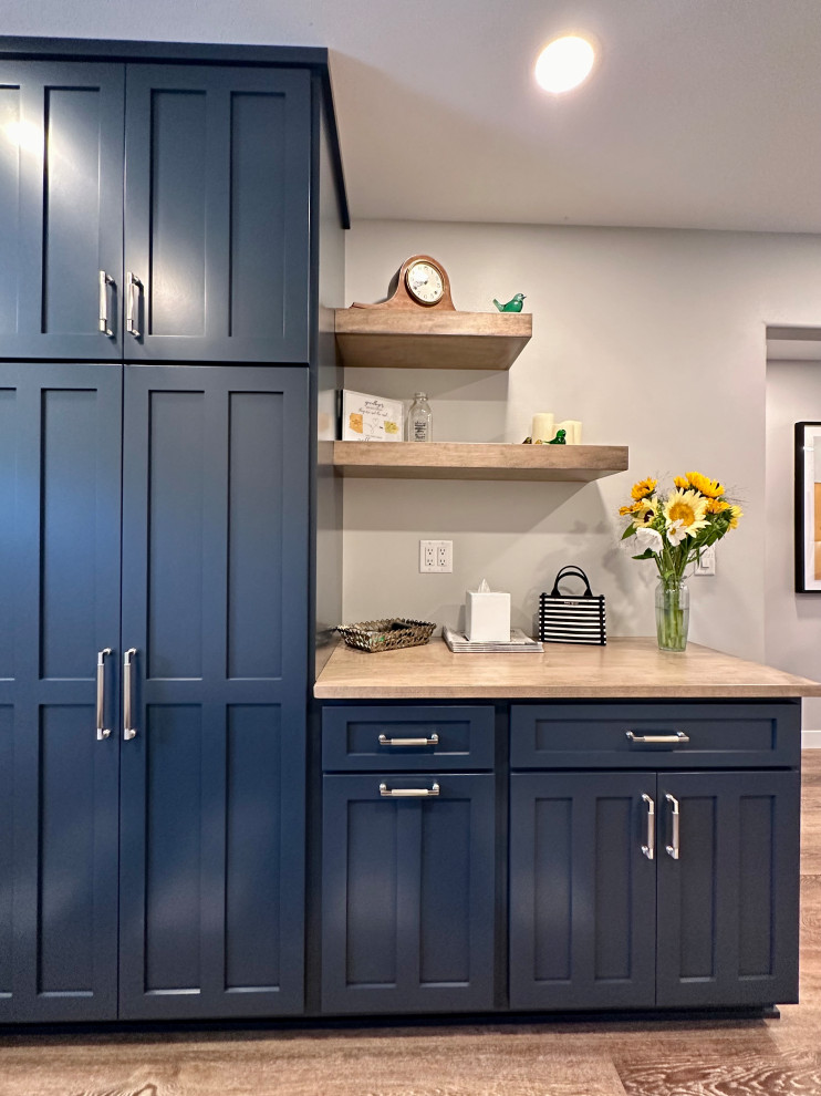 Utility room - mid-sized transitional single-wall medium tone wood floor and beige floor utility room idea with recessed-panel cabinets, blue cabinets, wood countertops, white walls, a stacked washer/dryer and beige countertops