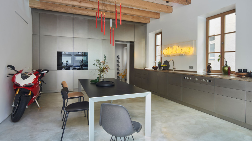 Esempio di una cucina lineare minimal con ante lisce, ante in acciaio inossidabile, top in granito, paraspruzzi bianco, elettrodomestici neri, pavimento grigio, top beige e travi a vista