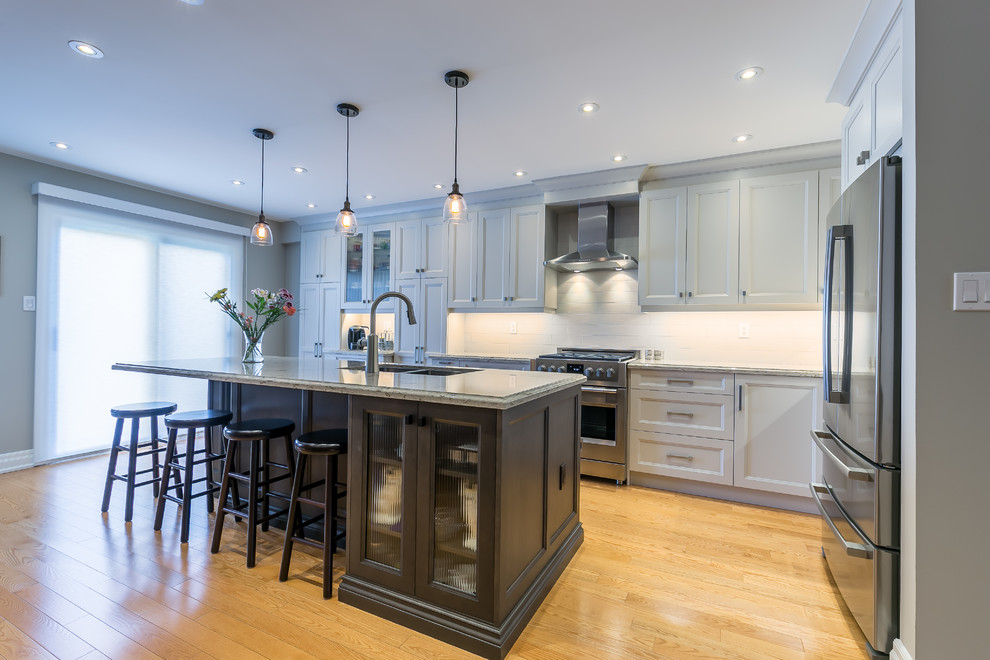 Kitchen - mid-sized transitional l-shaped brown floor kitchen idea in Toronto with a double-bowl sink, white cabinets, white backsplash, stainless steel appliances and an island