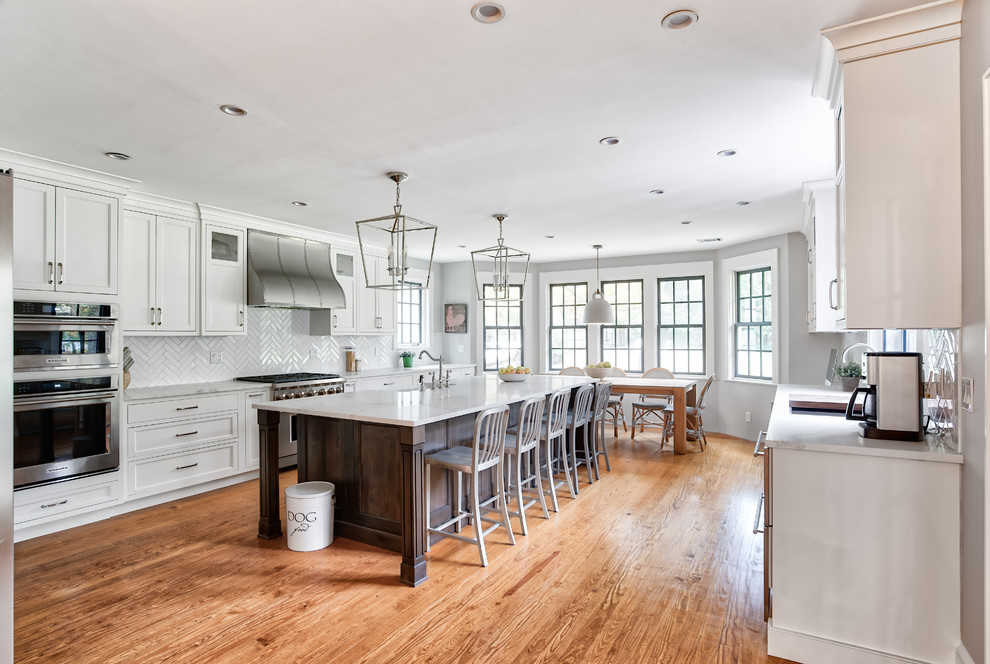 Inspiration for a huge timeless galley medium tone wood floor eat-in kitchen remodel in New York with a farmhouse sink, beaded inset cabinets, white cabinets, quartzite countertops, white backsplash, subway tile backsplash, stainless steel appliances, an island and white countertops