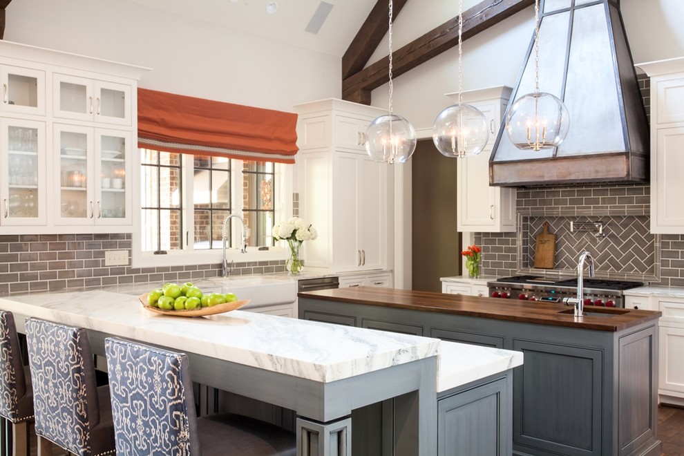 Transitional kitchen in Atlanta with a farmhouse sink, glass-front cabinets, white cabinets, wood benchtops, grey splashback, subway tile splashback, stainless steel appliances and multiple islands.