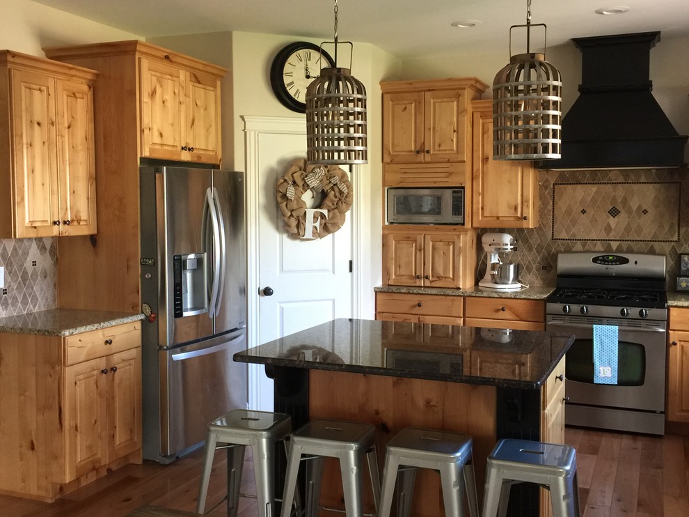 This is an example of a mid-sized country l-shaped kitchen in Austin with raised-panel cabinets, medium wood cabinets, granite benchtops, brown splashback, ceramic splashback, stainless steel appliances, dark hardwood floors, with island and brown floor.