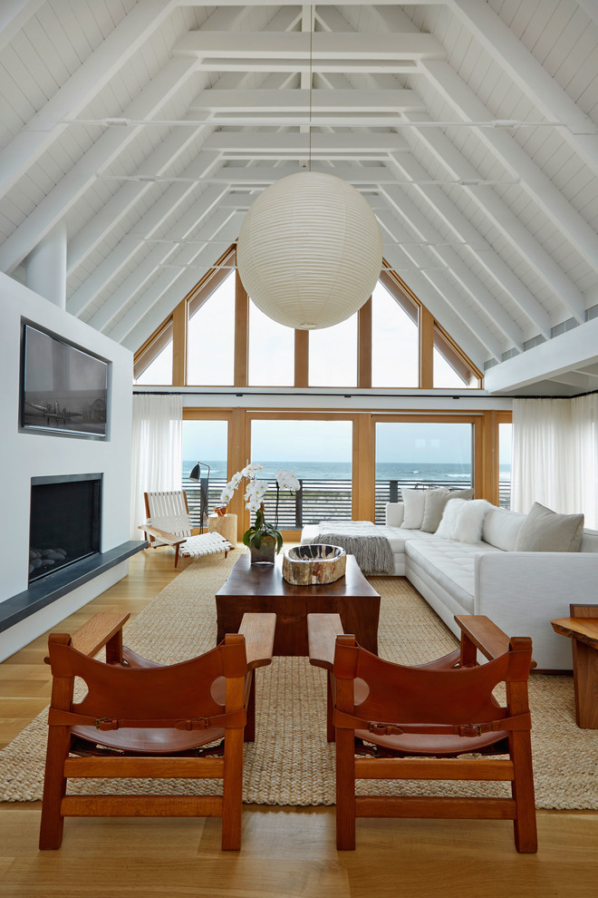 Inspiration for a large beach style open concept living room in New York with white walls, medium hardwood floors, a standard fireplace, a plaster fireplace surround, a wall-mounted tv and brown floor.