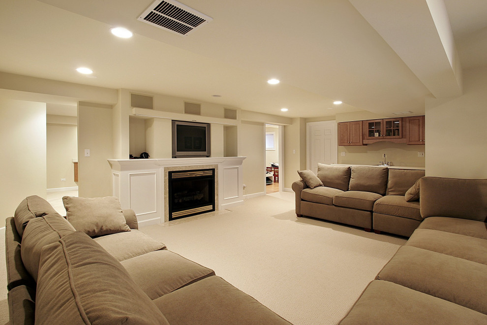 Exemple d'un grand sous-sol tendance donnant sur l'extérieur avec un mur beige, moquette, une cheminée standard, un manteau de cheminée en bois et un sol beige.