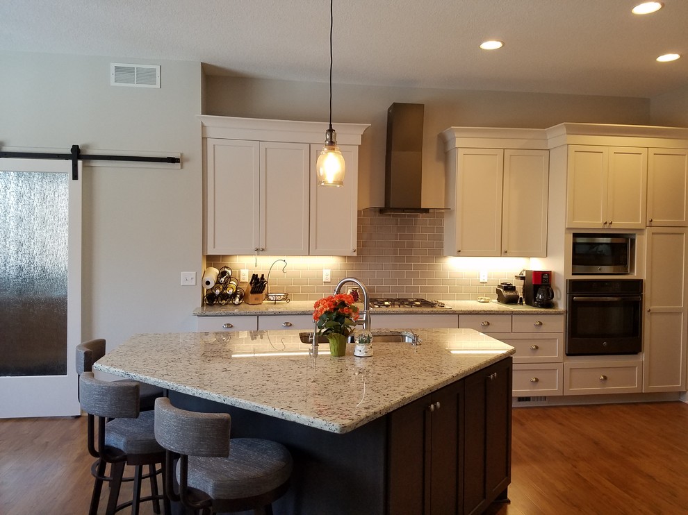 Mid-sized transitional galley eat-in kitchen in Minneapolis with an undermount sink, flat-panel cabinets, white cabinets, granite benchtops, beige splashback, ceramic splashback, stainless steel appliances, medium hardwood floors, with island and brown floor.